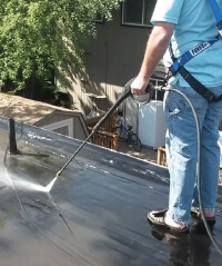 A contractor power washes an asphalt roof.