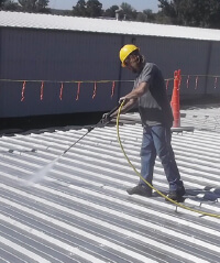 A contractor in a yellow hardhat sprays a metal roof with Inland's product.