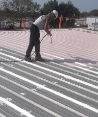 A contractor applies Inland's SEBS coating to a metal roof.