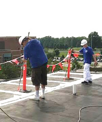 Contractors prepare a single ply roof to be coated.