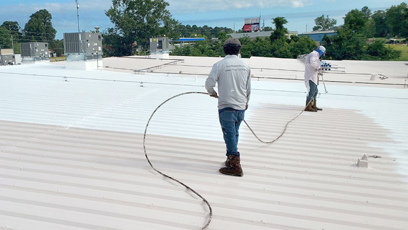 Workers spraying a roof coating to a metal commercial roof
