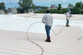 Workers spraying a roof coating to a metal commercial roof
